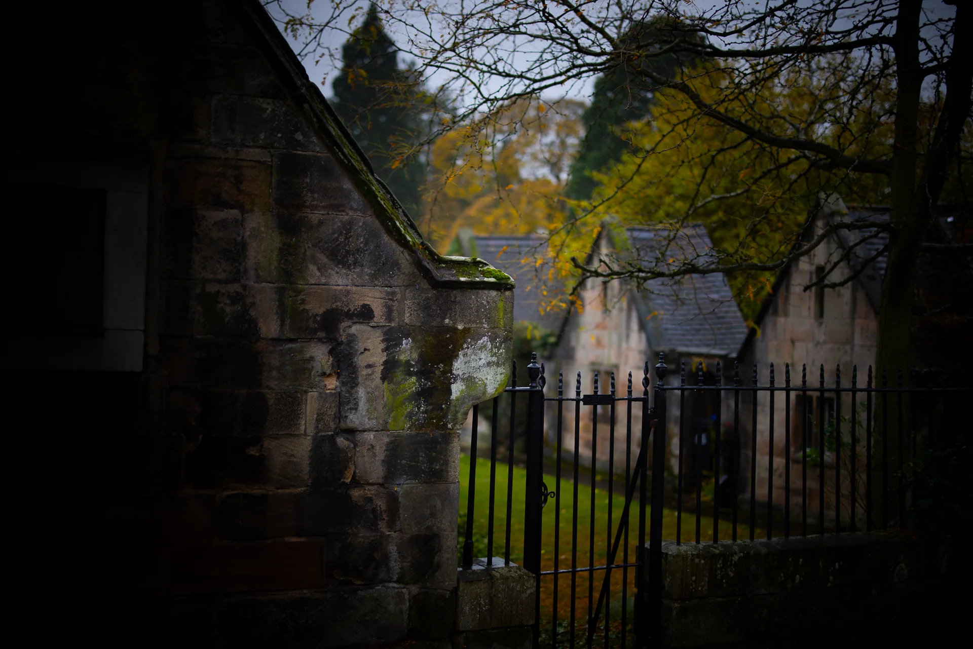 Historic stone buildings and an iron gate beneath trees